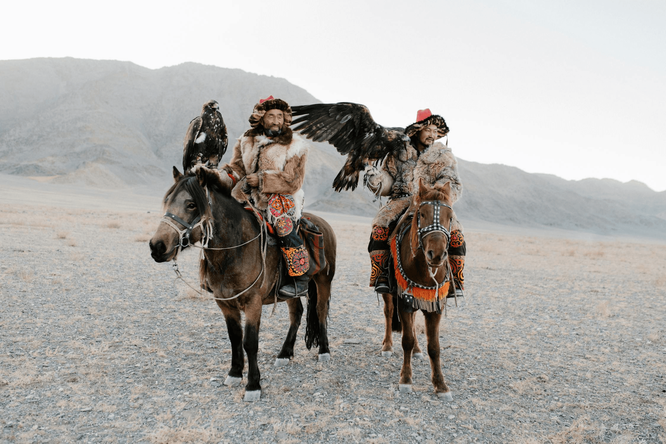 Two eagle hunters on horseback with golden eagles in a mountain valley
