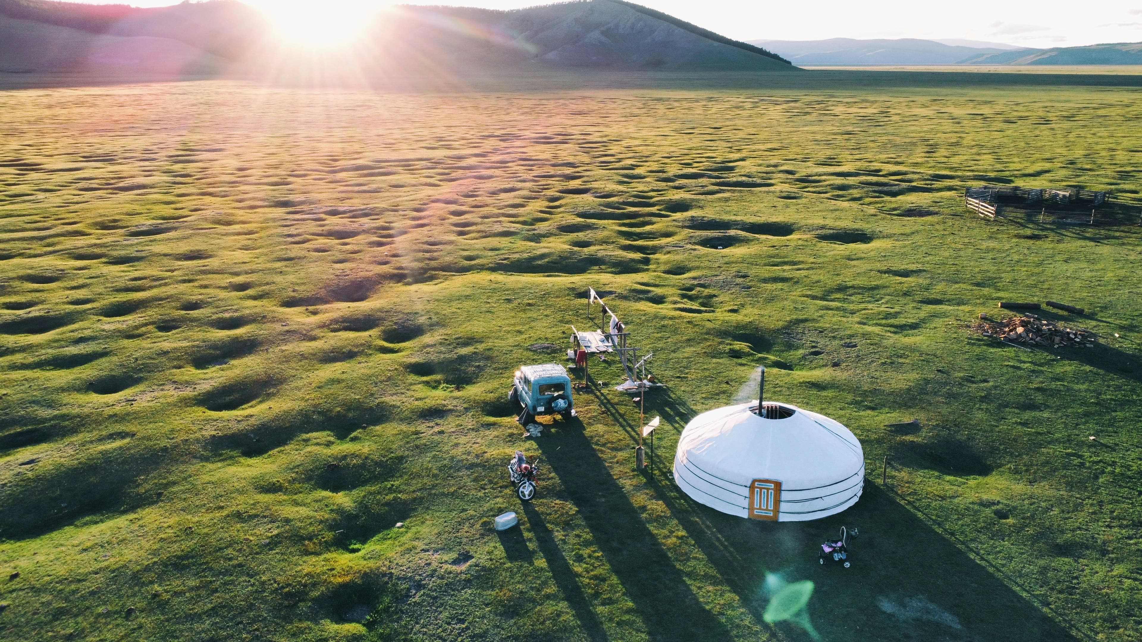 Aerial view of a herder's ger and truck on green summer pasture at sunset